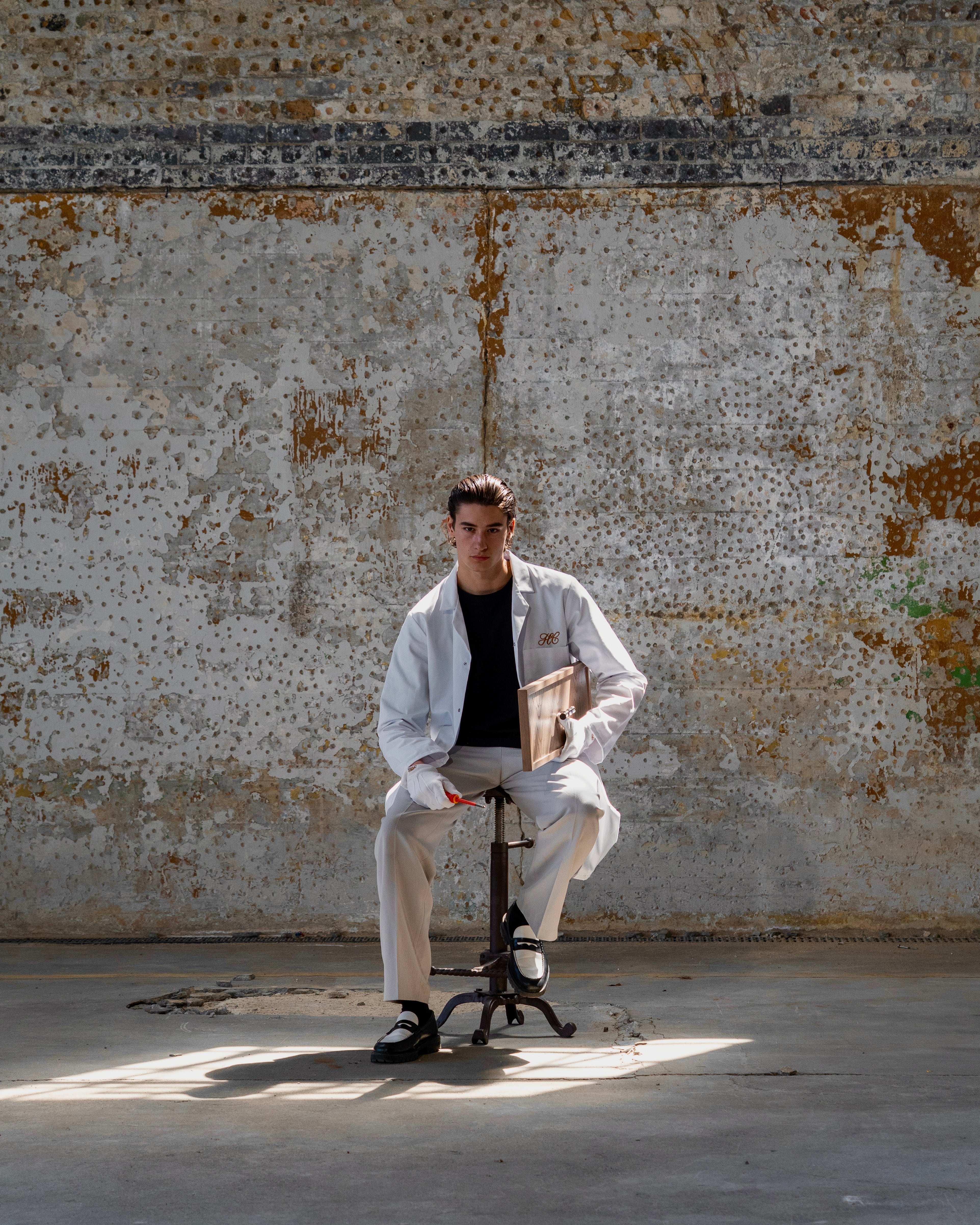 Person sitting on a small stool against a textured wall.