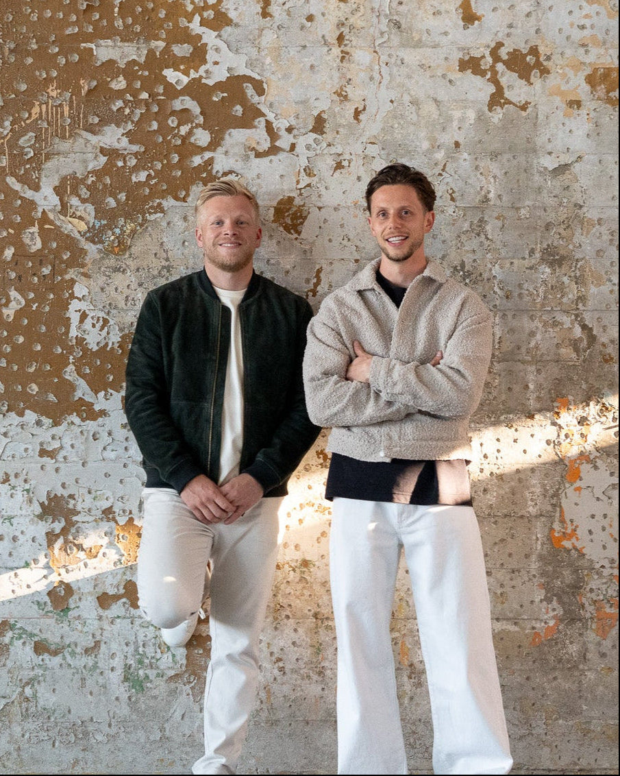 Two men standing against a textured wall with peeling paint.