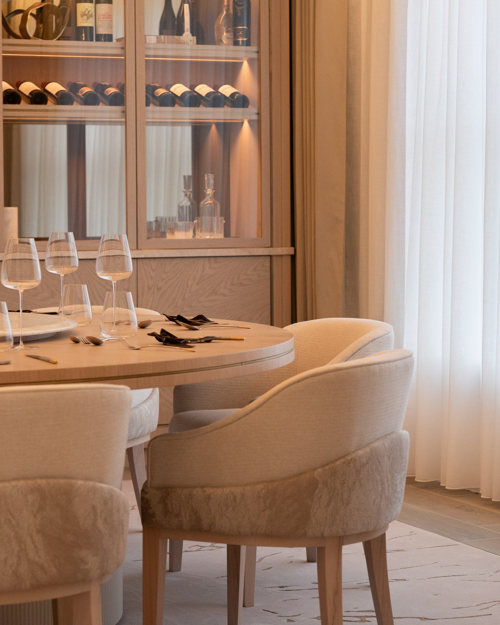 Luxury dining room featuring bespoke dining table, upholstered chairs and illuminated wine cabinet.