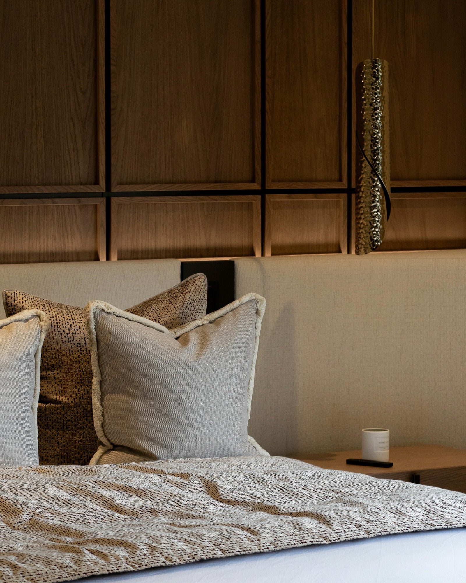 Detail of bespoke upholstered bed and walnut feature wall in a luxury bedroom